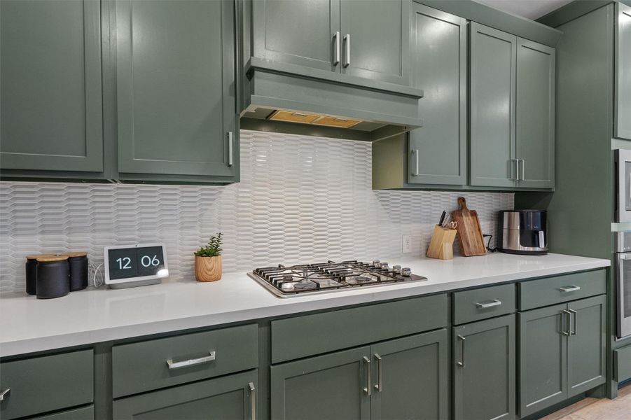 Kitchen featuring green cabinets, stainless steel appliances, and decorative backsplash
