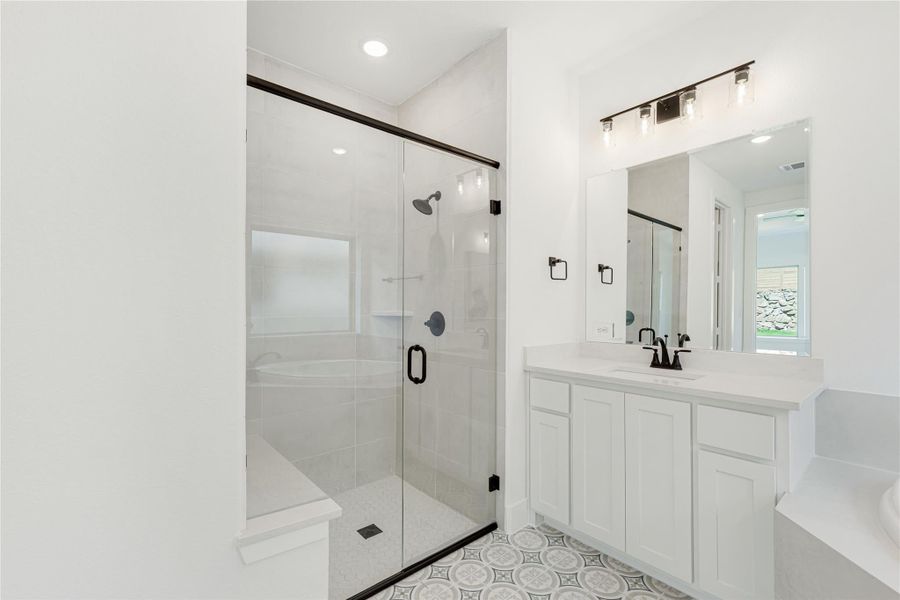 Bathroom with glass walk-in shower, soaking tub, white vanity, and patterned tile floor