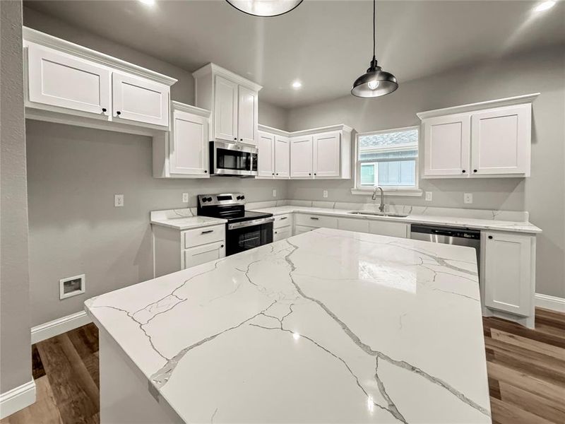 Kitchen with a kitchen island, stainless steel appliances, light stone counters, white cabinets, and recessed lighting