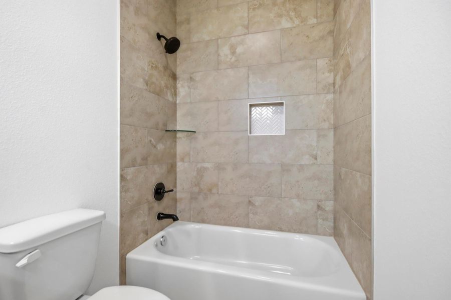 Modern bathroom featuring a sleek tub surrounded by elegant tile, complete with a built-in shelf for convenience.