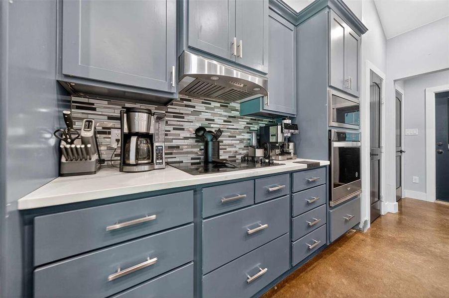 Kitchen with concrete flooring, tasteful backsplash, under cabinet range hood, appliances with stainless steel finishes, and gray cabinetry Kitchen with concrete flooring, tasteful backsplash, under cabinet range hood, appliances with stainless steel finishes, and gray cabinetry