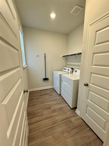 Dedicated utility room featuring wood-finish flooring, overhead shelving, and a window with blinds