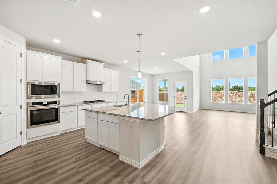 Kitchen featuring stainless steel appliances, light wood finished floors, recessed lighting, a center island with sink, and white cabinetry Kitchen featuring stainless steel appliances, light wood finished floors, recessed lighting, a center island with sink, and white cabinetry