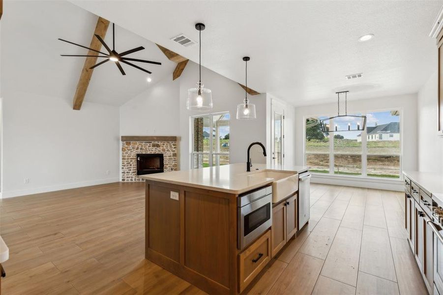 Kitchen with lofted ceiling with beams, light hardwood / wood-style flooring, a brick fireplace, sink, and a kitchen island with sink