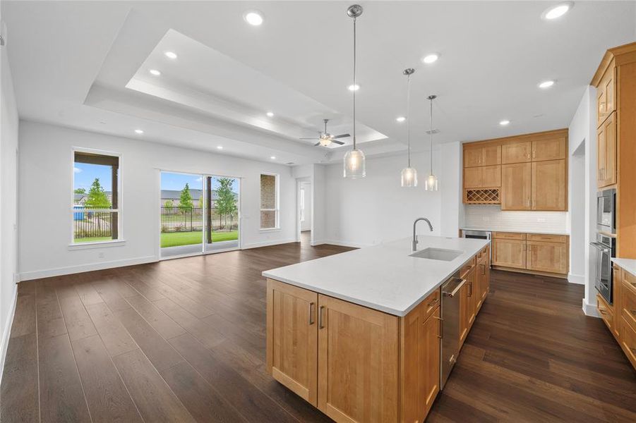 Open-concept living space featuring wood-finish flooring, a tray ceiling with recessed lighting, and a kitchen island with pendant lighting