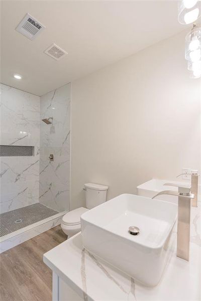 Bathroom featuring tiled shower, vanity, hardwood / wood-style flooring, and toilet