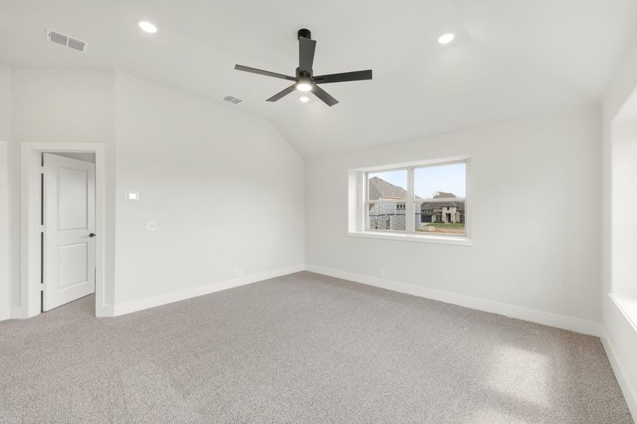 Empty bedroom with vaulted ceiling, black ceiling fan, gray carpet, and a window with neighborhood view