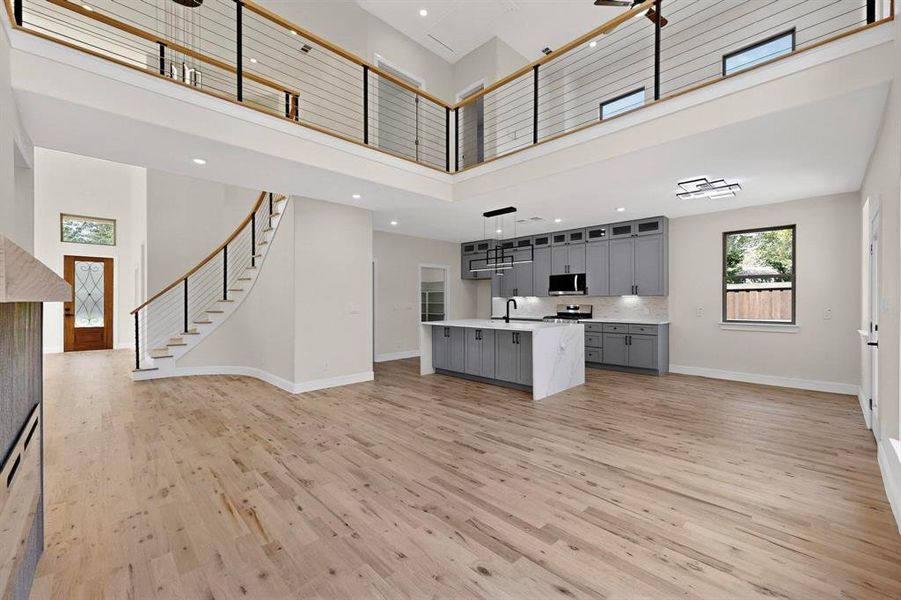 Kitchen featuring gray cabinetry, open floor plan, light wood-style floors, glass insert cabinets, and a high ceiling Kitchen featuring gray cabinetry, open floor plan, light wood-style floors, glass insert cabinets, and a high ceiling