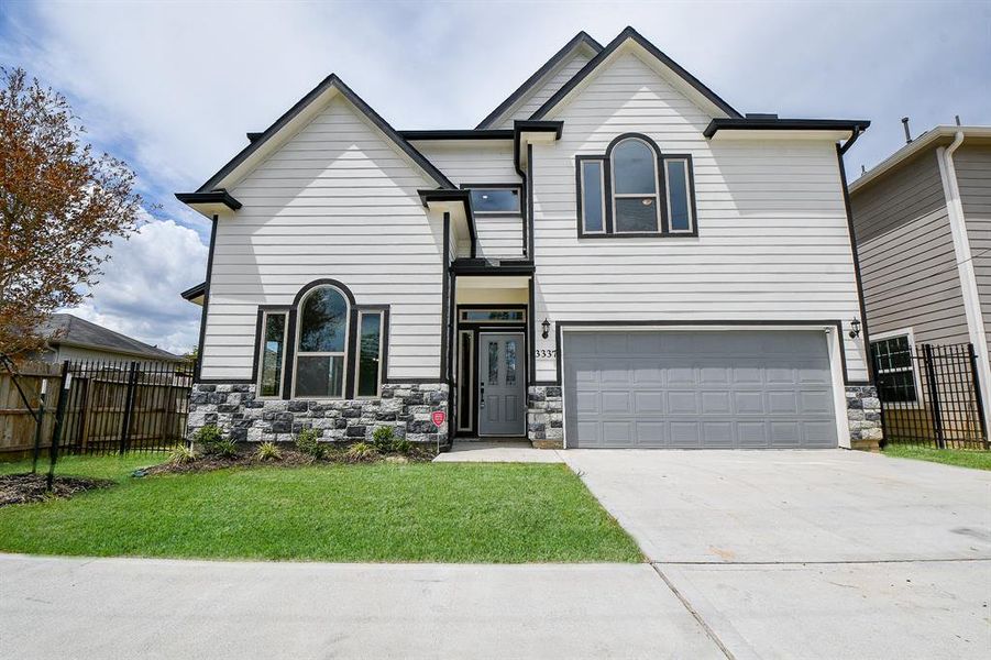 Modern two-story home with a mix of stone and siding exterior, featuring large windows, a two-car garage, and a neatly landscaped front yard.