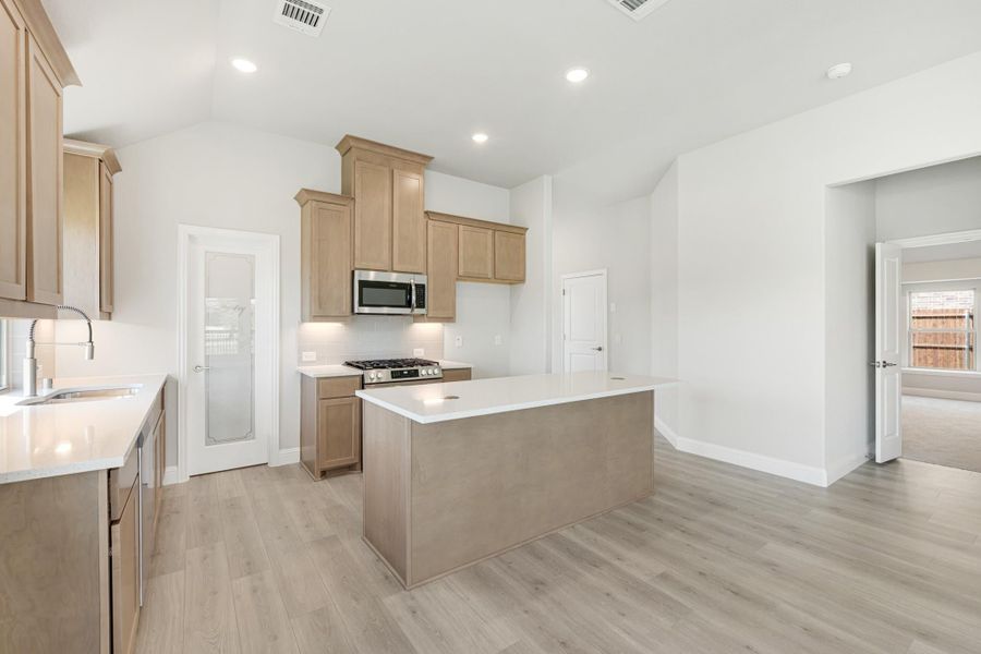 Kitchen with light wood cabinets, center island, stainless steel appliances, and light hardwood floors