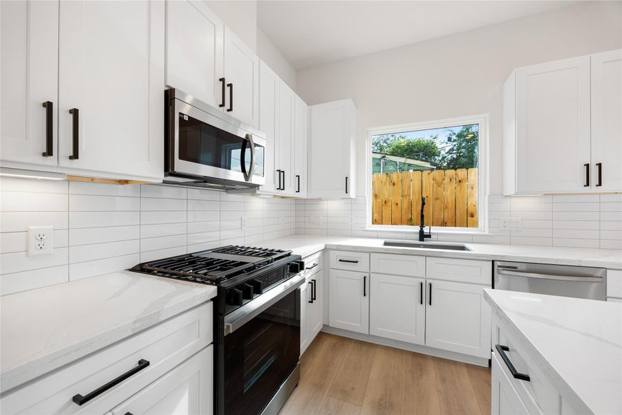 The kitchen comes equipped with stainless steel appliances, quartz countertops, beautiful white cabinetry and modern backsplash, high ceilings with recessed lighting, kitchen island with pendant lighting, and large window over the sink for natural lighting.