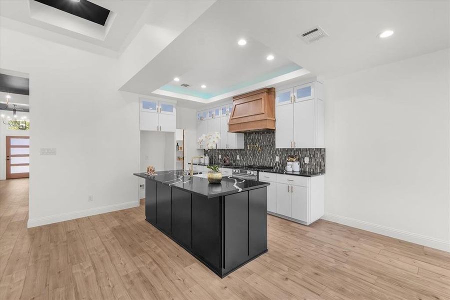 Kitchen with white cabinets, glass insert cabinets, decorative backsplash, a tray ceiling, and recessed lighting