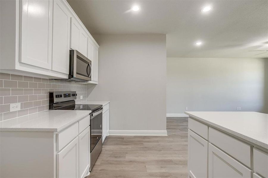 Kitchen with appliances with stainless steel finishes, decorative backsplash, light wood-style flooring, recessed lighting, and light countertops Kitchen with appliances with stainless steel finishes, decorative backsplash, light wood-style flooring, recessed lighting, and light countertops