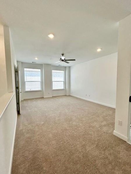 Spacious room featuring neutral carpeting, multiple windows with blinds, recessed lighting, a ceiling fan, and white baseboards