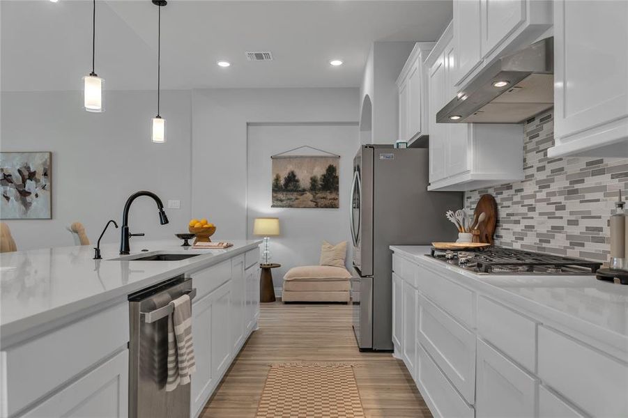 Kitchen with white cabinets, tasteful backsplash, hanging light fixtures, appliances with stainless steel finishes, and light stone counters Kitchen with white cabinets, tasteful backsplash, hanging light fixtures, appliances with stainless steel finishes, and light stone counters