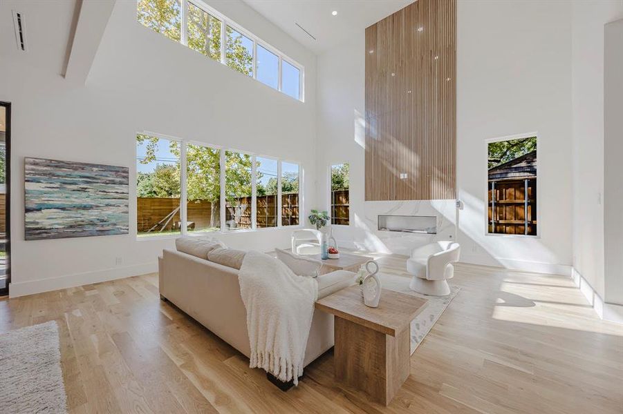 Living room with plenty of natural light, light wood-type flooring, a high ceiling, and a high end fireplace Living room with plenty of natural light, light wood-type flooring, a high ceiling, and a high end fireplace