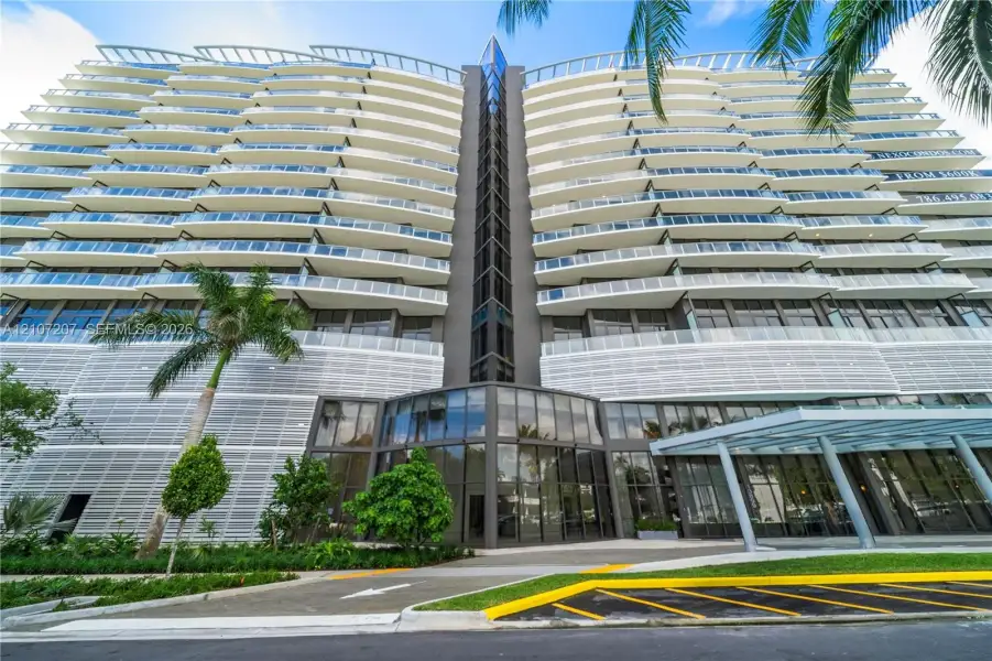 Contemporary high-rise architecture featuring expansive glass balconies, floor-to-ceiling windows, louvered exterior screening, and a prominent glass-enclosed entryway Contemporary high-rise architecture featuring expansive glass balconies, floor-to-ceiling windows, louvered exterior screening, and a prominent glass-enclosed entryway