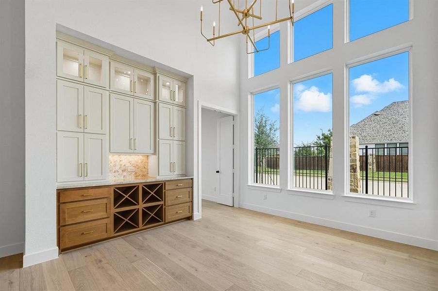 Bar area featuring brown cabinetry, a chandelier, glass insert cabinets, hanging light fixtures, and light wood finished floors Bar area featuring brown cabinetry, a chandelier, glass insert cabinets, hanging light fixtures, and light wood finished floors