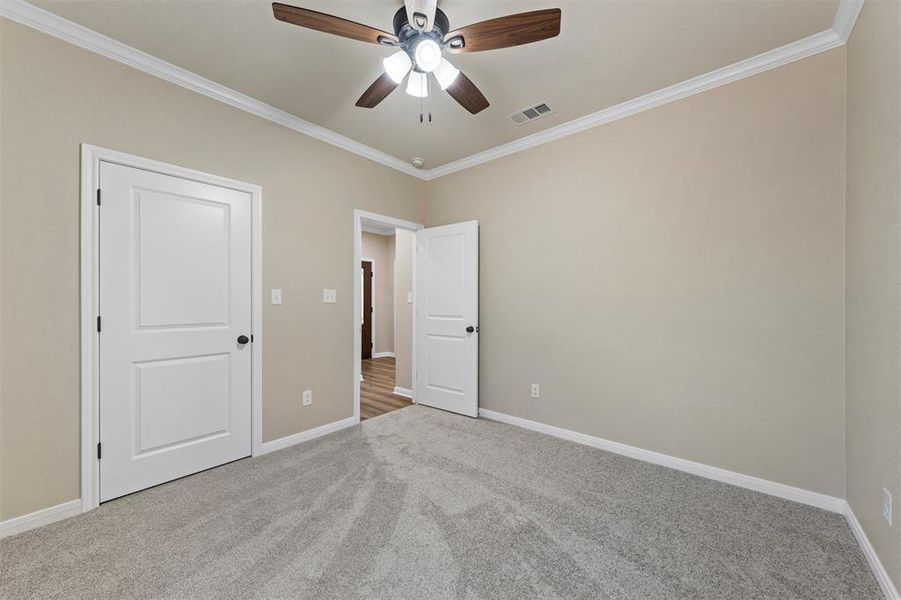 Unfurnished bedroom featuring carpet flooring, ornamental molding, and a ceiling fan