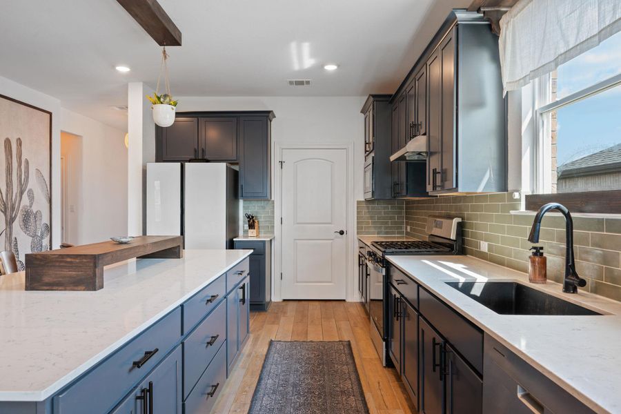 Kitchen with light stone countertops, appliances with stainless steel finishes, light wood-style floors, backsplash, and under cabinet range hood Kitchen with light stone countertops, appliances with stainless steel finishes, light wood-style floors, backsplash, and under cabinet range hood