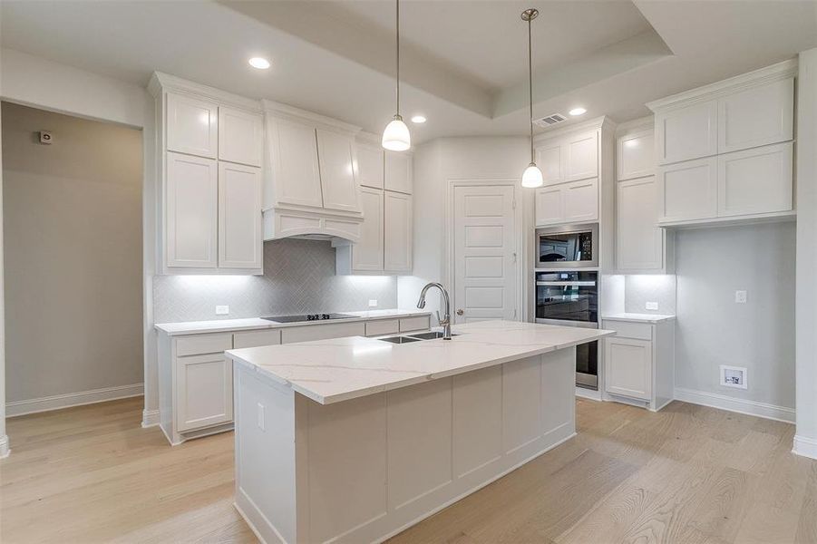 Kitchen featuring light hardwood / wood-style floors, stainless steel microwave, decorative backsplash, and a tray ceiling