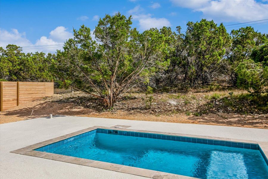 A tranquil inground pool with a spacious patio offers serene relaxation and natural privacy.