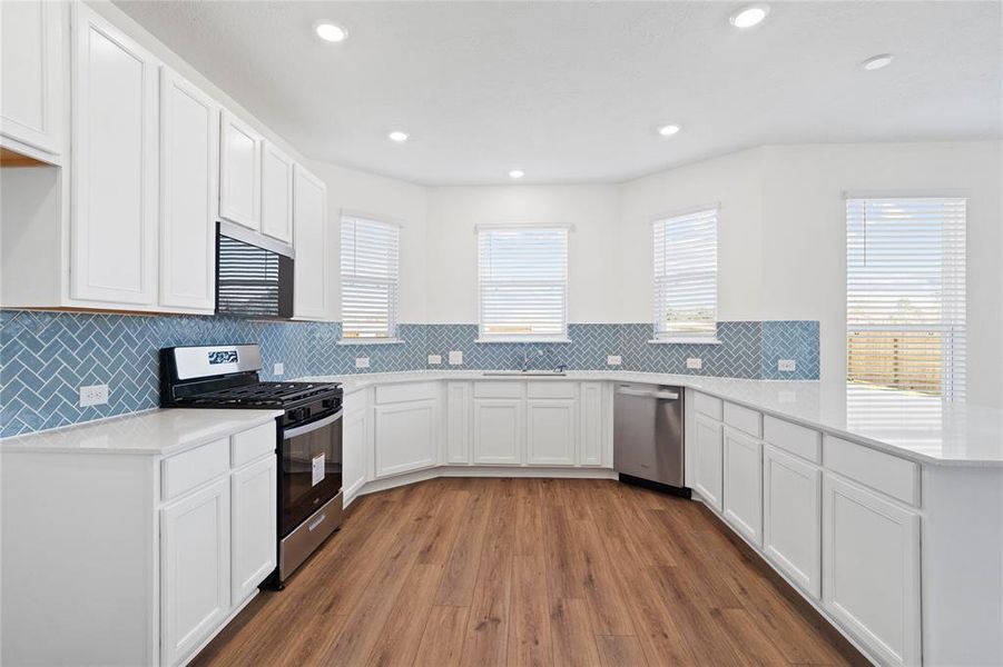 Another view of this spacious kitchen featuring large windows with privacy blinds, high ceilings with recessed lighting, stained cabinets with silestone countertops, SS appliances, modern tile backsplash, extended countertop for breakfast bar, and a walk-in pantry all overlooking your huge family room.