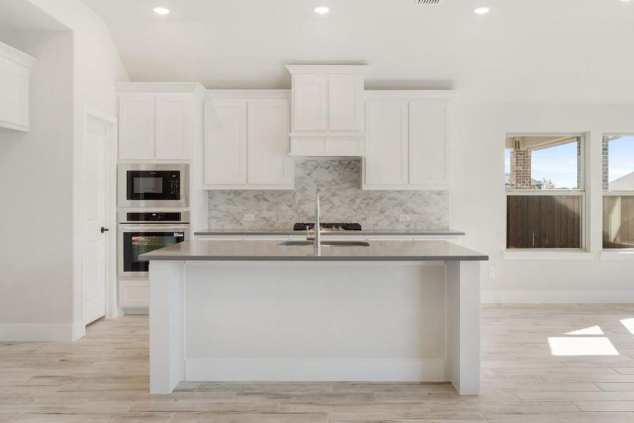 Kitchen with white cabinets, gray countertop island, marble tile backsplash, and stainless steel appliances Kitchen with white cabinets, gray countertop island, marble tile backsplash, and stainless steel appliances