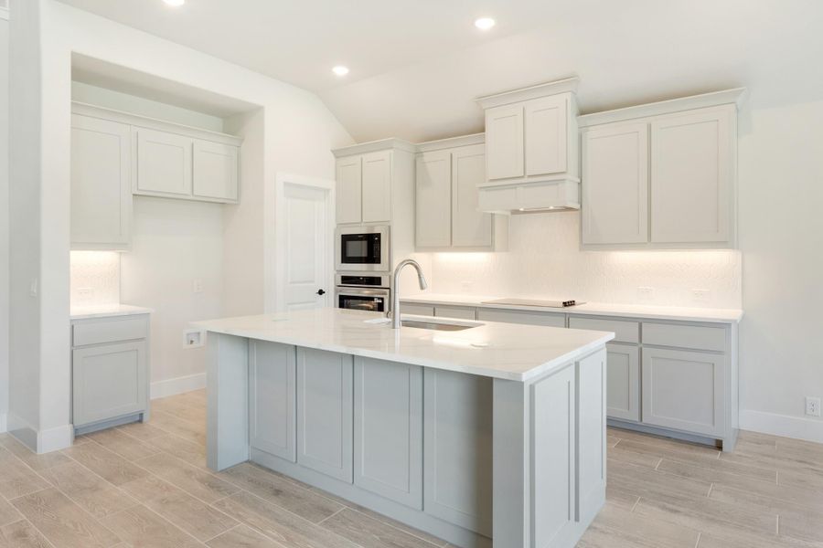 Kitchen with gray cabinets, center island with sink, white countertops, and stainless steel wall oven and microwave