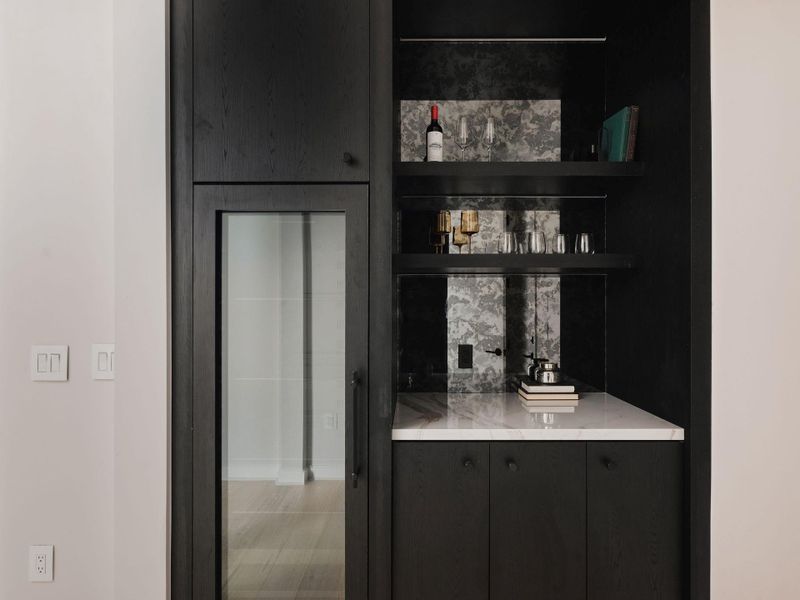 Built-in beverage station featuring dark wood-finish cabinetry, a white marble countertop, and open shelving with an antiqued mirror backsplash