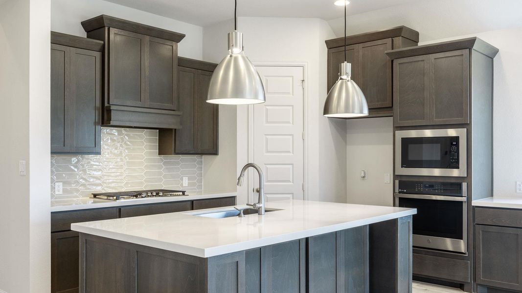Kitchen featuring stainless steel appliances, a sink, tasteful backsplash, light countertops, and dark brown cabinets Kitchen featuring stainless steel appliances, a sink, tasteful backsplash, light countertops, and dark brown cabinets