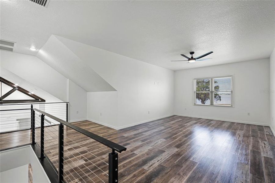 The room features high vaulted ceilings and large windows that fill the space with natural light, emphasizing the spacious feel. The sleek, wood-look flooring adds warmth and elegance to the room, complementing the clean, white walls perfectly.