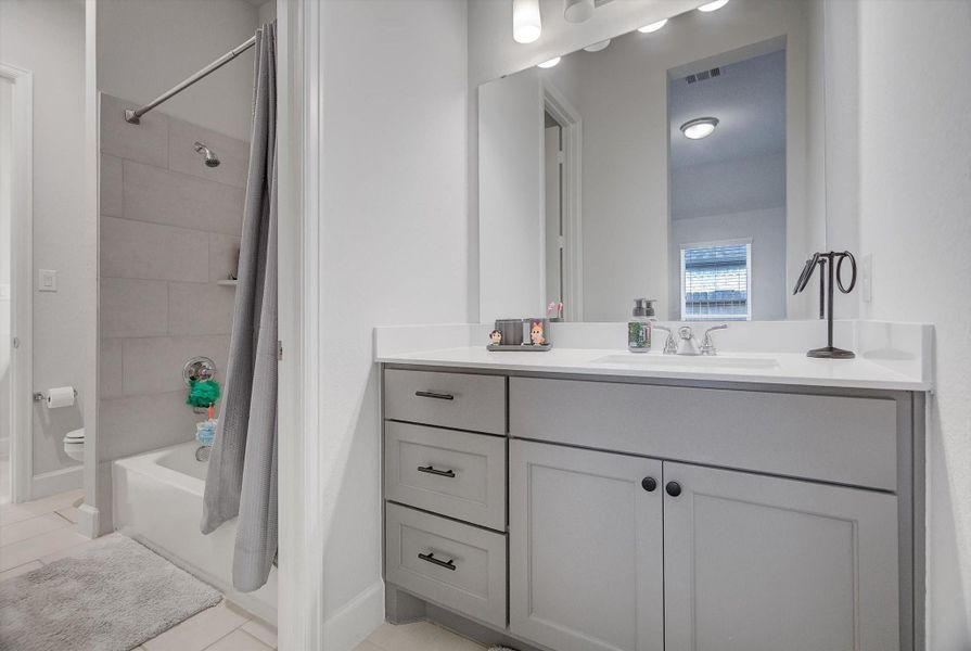 The secondary bedroom connects to a beautifully appointed Hollywood bath, complete with a private vanity offering soft-close cabinets and drawers, enhanced by bright, flattering lighting.