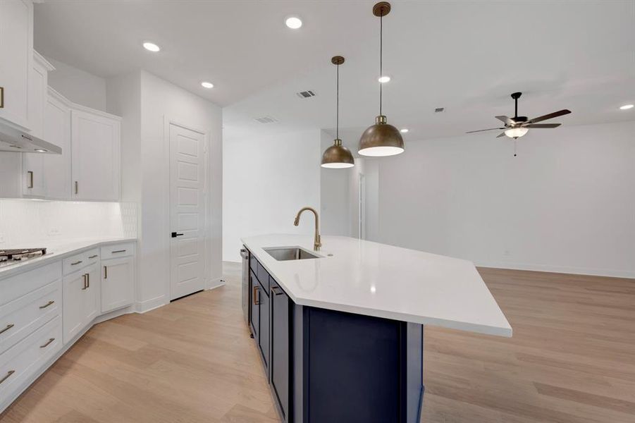 Kitchen with two tone cabinets, light wood-style flooring, hanging light fixtures, a center island with sink, and ceiling fan