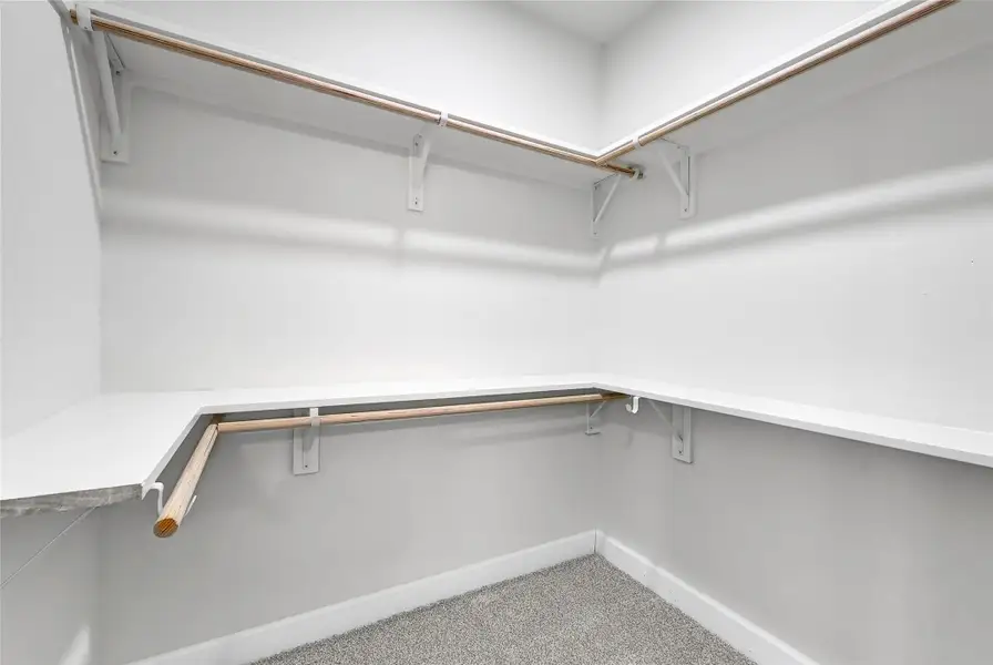 This is a spacious walk-in closet with clean white walls, ample shelving, and hanging rods, ideal for organized storage. The carpeted floor adds a cozy touch.