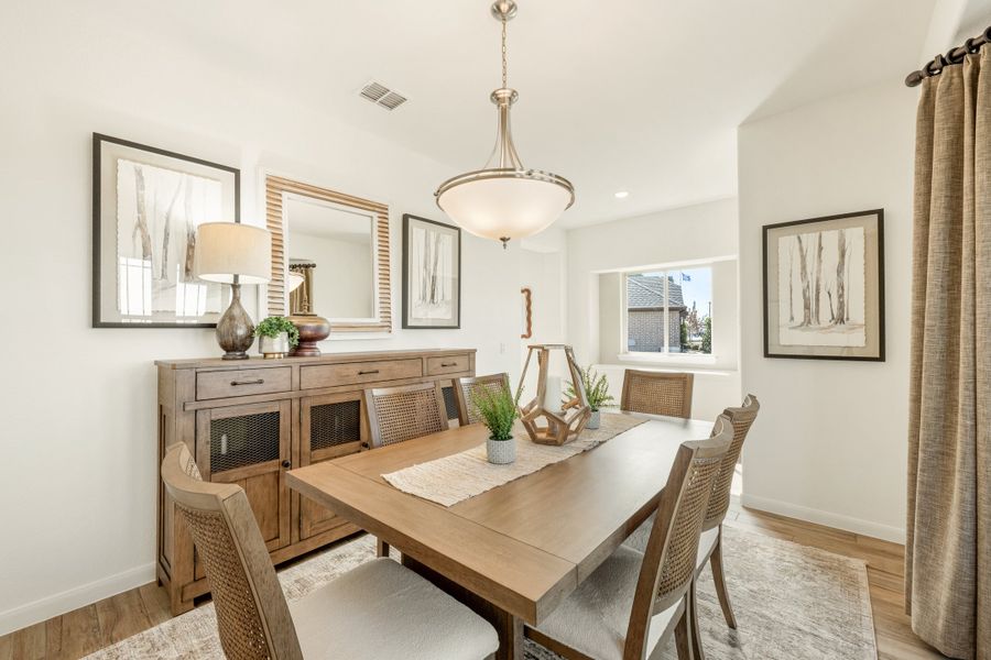 Dining room with wood table, woven chairs, pendant light, and wood sideboard on light hardwood floors