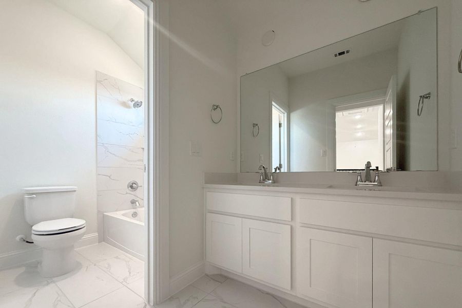 Bathroom featuring a dual vanity with white cabinetry, a large frameless mirror, and a combination shower-tub with a tiled surround Bathroom featuring a dual vanity with white cabinetry, a large frameless mirror, and a combination shower-tub with a tiled surround