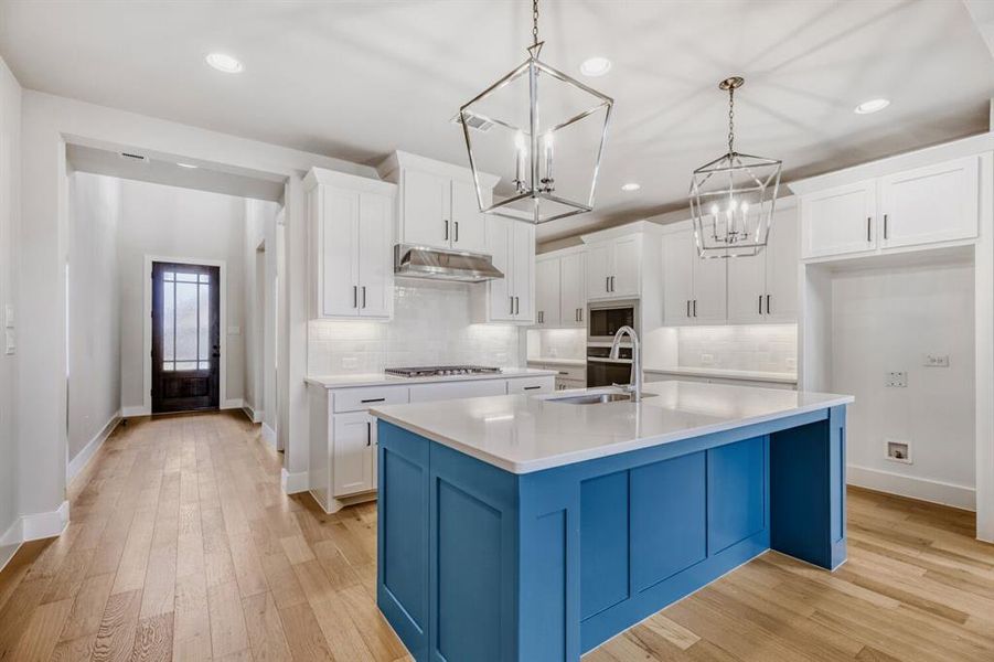 Dual tone kitchen with light wood finished floors, dual tone cabinetry, a kitchen island with sink, light stone counters, and decorative backsplash