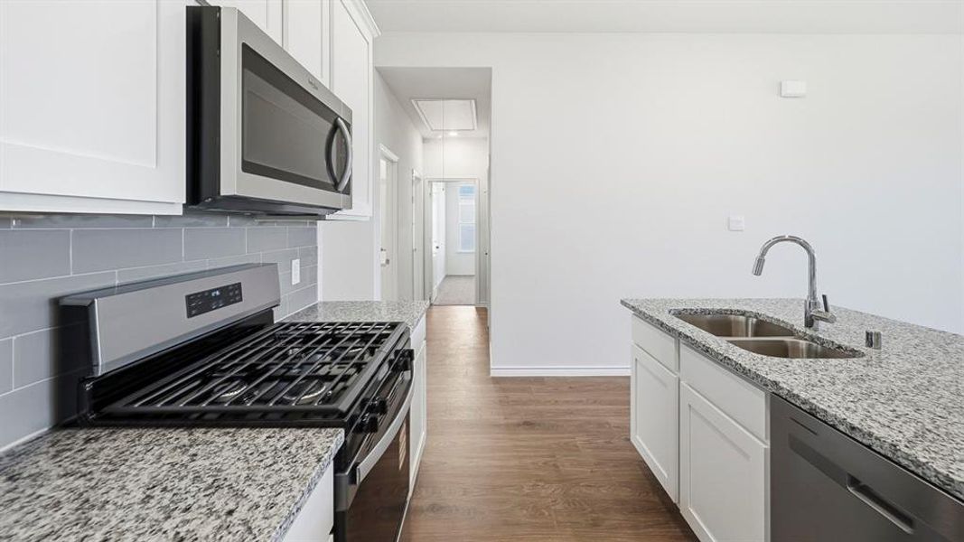 Kitchen with stainless steel appliances, white cabinets, dark wood-style floors, light stone counters, and decorative backsplash