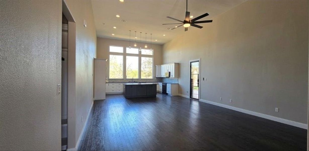 Unfurnished living room with dark wood flooring, a ceiling fan, 15 ft high ceiling, and recessed lighting Unfurnished living room with dark wood flooring, a ceiling fan, 15 ft high ceiling, and recessed lighting
