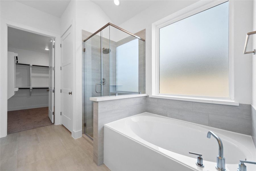 This alternate view of the primary bathroom showcases a walk-in shower with a stylish tile surround, a separate garden tub perfect for unwinding after a long day, and a large rain glass window that provides natural light while maintaining privacy.