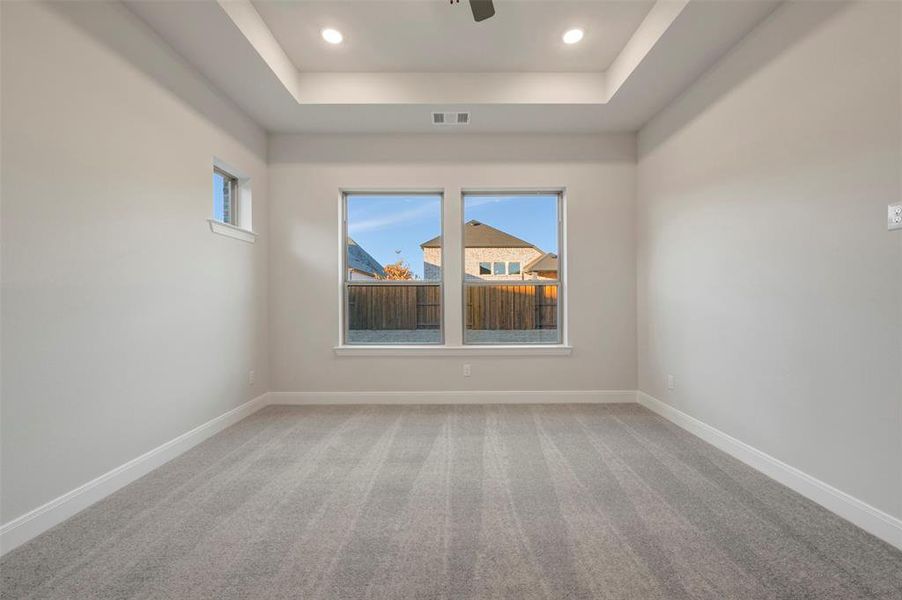 Spare room featuring light carpet, healthy amount of natural light, a raised ceiling, recessed lighting, and a ceiling fan