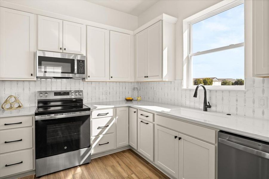 Kitchen featuring white shaker cabinetry, stainless steel appliances, a tile backsplash, light-toned countertops, and wood-finish flooring