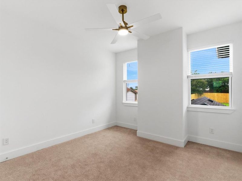 Carpeted room featuring white walls, a gold-finished ceiling fan with integrated lighting, two windows with white blinds, and white baseboards