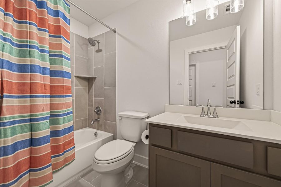 This bathroom features a modern design with a vanity and large mirror, a tub-shower combo with neutral tile, and a colorful striped shower curtain. The space is well-lit with stylish lighting fixtures.