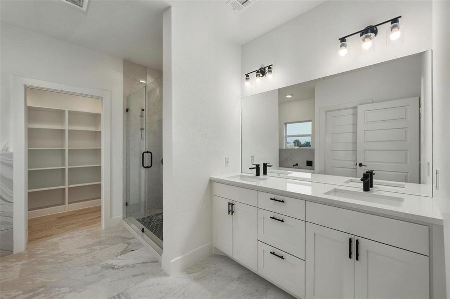 Full bathroom with a shower stall, double vanity, marble finish flooring, and a spacious closet