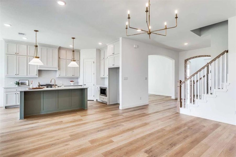 Kitchen with arched walkways, a center island with sink, decorative light fixtures, light wood-style flooring, and recessed lighting Kitchen with arched walkways, a center island with sink, decorative light fixtures, light wood-style flooring, and recessed lighting