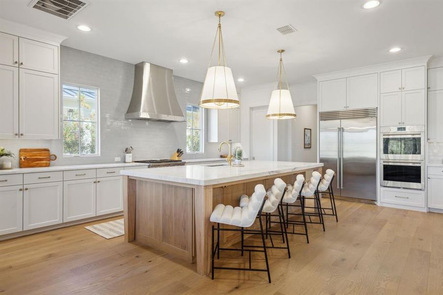 Kitchen featuring light wood-style floors, wall chimney exhaust hood, visible vents, and appliances with stainless steel finishes Kitchen featuring light wood-style floors, wall chimney exhaust hood, visible vents, and appliances with stainless steel finishes