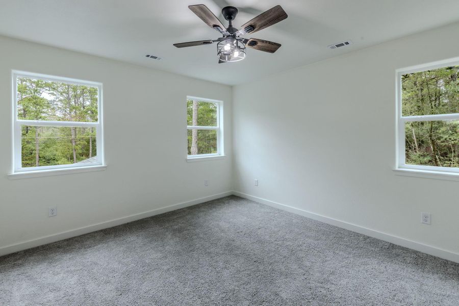 Well-lit sleeping quarters with plush carpeting and a modern ceiling fan, offering tranquil tree-lined views. Well-lit sleeping quarters with plush carpeting and a modern ceiling fan, offering tranquil tree-lined views.