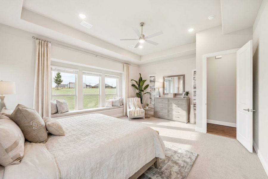 Master bedroom with tray ceiling, ceiling fan, window seat, and neutral carpet flooring